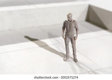 Miniature 3d printed monochrome figure of a man in leisurewear standing on tiles casting a shadow in the sunlight with copyspace