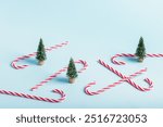 Miniature artificial Christmas trees and red Christmas candy canes on blue background.Christmas background, congratulation.Selective focus.