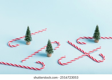 Miniature artificial Christmas trees and red Christmas candy canes on blue background.Christmas background, congratulation.Selective focus. - Powered by Shutterstock