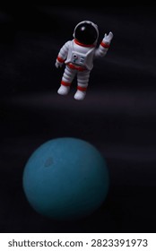 A miniature astronaut appears to float in space waving above a glowing blue planet