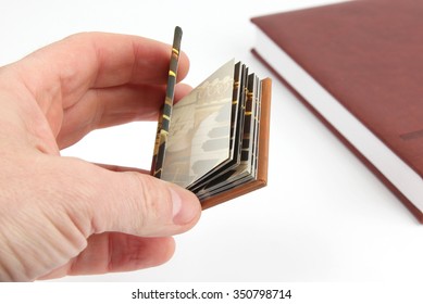 Miniature Book In Hand On A Background Of The Usual Books
