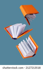 miniature books in an orange cover fly on a blue background - Shutterstock ID 2127213518