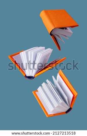 miniature books in an orange cover fly on a blue background