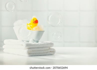 A miniature bubble bath yellow rubber duck and white towels on bathroom countertop, children bath accessories, baby care, space for text