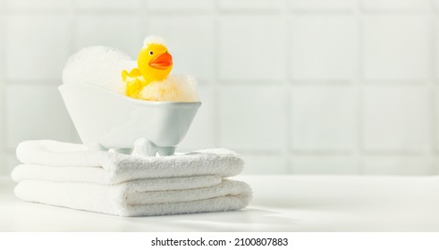 A miniature bubble bath, yellow rubber duck and white towels on bathroom countertop, children bath accessories, baby care, space for text - Shutterstock ID 2100807883