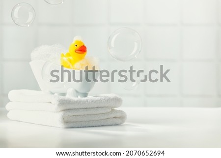 A miniature bubble bath yellow rubber duck and white towels on bathroom countertop, children bath accessories, baby care, space for text