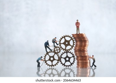 Miniature businessman on top of a pile of coins with construction workers, leadership, success, inequality concept