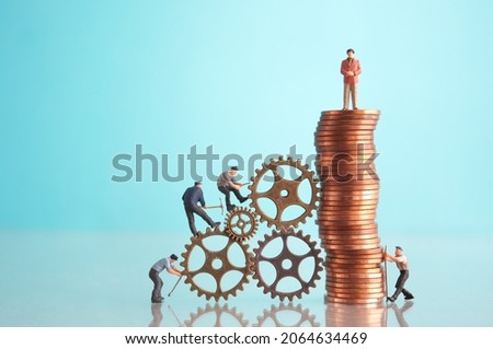 Miniature businessman on top of a pile of coins with construction workers, leadership, success concept