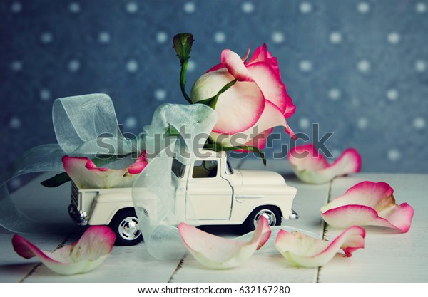 Miniature car carrying\
pink rose flower.