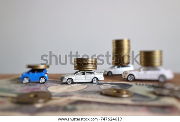 Miniature car help carry rolls\
of coins in increasing level and money on wood table in white\
background