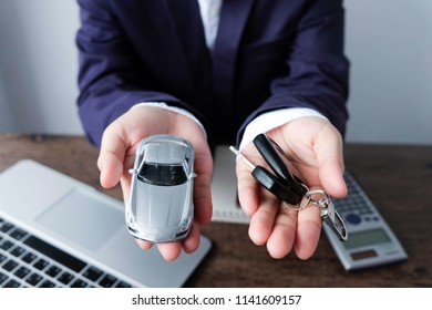 Miniature Car Model And Key On Hand With Laptop And Calculator On Wooden Table, Auto Dealership And Rental Concept
