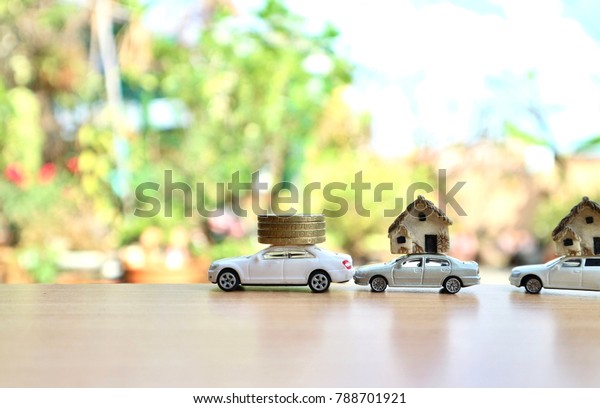 Miniature cars help carry roll coins and houses on wood\
table in blur natural tree bright light, save money for home\
concept                 \
