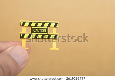 Miniature Caution Barricade Held Between Fingers Symbolizing Warning