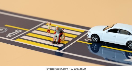 A Miniature Child With A Hand Raised And A Miniature Man  In A Wheelchair Crossing A Crosswalk.