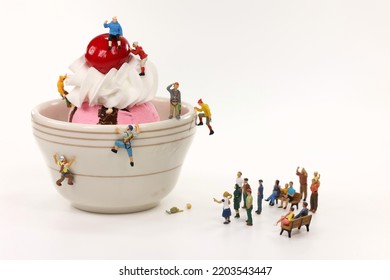 Miniature climbers ascend a bowl of ice cream with an audience. - Shutterstock ID 2203543447