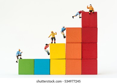 Miniature Climbers Team Climbing On Stack Of Cube Building Blocks