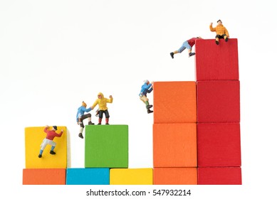 Miniature Climbers Team Climbing On Stack Of Cube Building Blocks