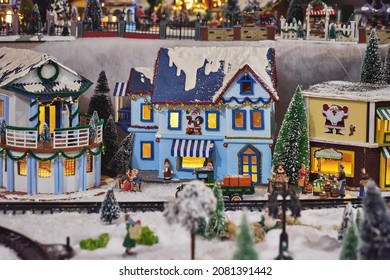 Miniature colored houses and figures of people during celebration of Christmas, snowy streets, and glowing lanterns. Miniature toy city during winter season. City scene in miniature models