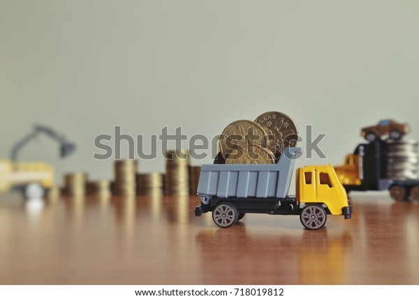 Miniature construction truck carry\
dollar Singapore coins and blur loader with rolls ladder of gold\
money and car working on wood table in light yellow\
tone