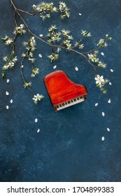 Miniature copie of the piano with blossoming cherry tree branches. Top view, close-up on classic blue background	