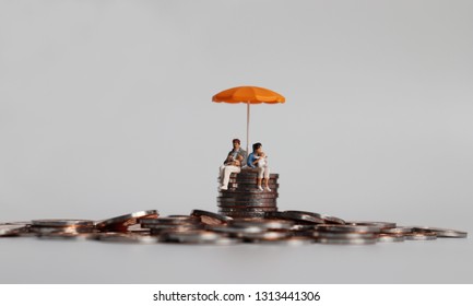 A miniature couple holding a baby sitting with an orange umbrella on a pile of coins.