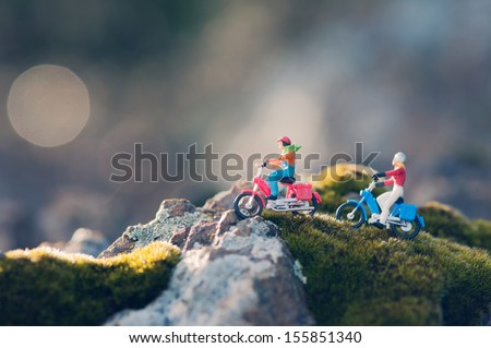 Miniature couple traveling through the countryside on vintage motorcycles at dawn. Macro photography