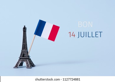 a miniature of the Eiffel Tower, a french flag and the text bon 14 juillet, happy 14 july, the national day of France written in French, against a pale blue background