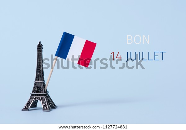 a miniature of the\
Eiffel Tower, a french flag and the text bon 14 juillet, happy 14\
july, the national day of France written in French, against a pale\
blue background
