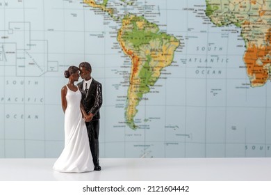 Miniature figure of beautiful dark skin bride and groom. Blurred map of South America in the background. Honeymoon, romantic travel or Valentines day concept. Copy space