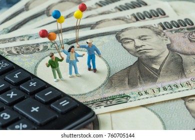 Miniature Figure Happy Family Holding Balloons Standing On Pile Of Japanese Yen Banknotes With Black Calculator As Financial Happy Investment Concept.