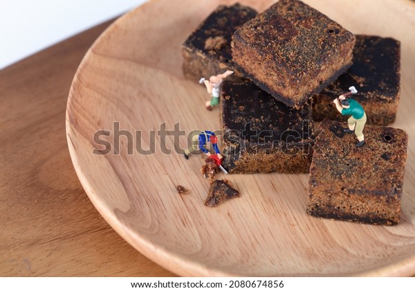 Miniature figures breaking down brown sugar cubes\
on a plate