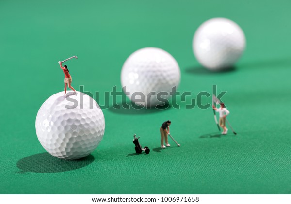 Miniature figures of golfers playing a round of golf\
with one putting for the hole and flag an d the other teeing-off\
from on top of a golf\
ball