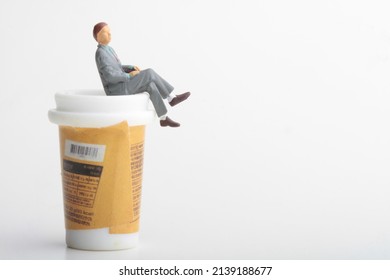 miniature figurine of a business man sitting on the top of a giant cup of coffee 