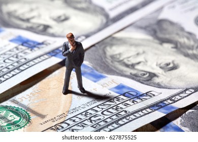 Miniature figurine businessman with 100 dollars banknote on background. Concept - Shutterstock ID 627875525