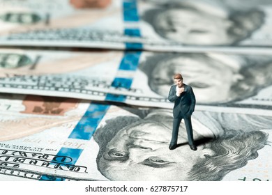 Miniature figurine businessman with 100 dollars banknote on background. Concept - Shutterstock ID 627875717