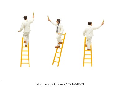 Miniature Figurine Character As Painter Standing On Wooden Ladder And Painting Wall With Paint Tools Isolated On White Background.