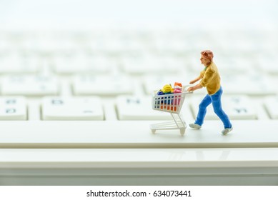 Miniature Figurine : A Male Shopper Pushes A Shopping Cart On A Space Bar On White Keyboard. Concept Of Brick And Mortar Stores Nowadays Face With Increased Competition From Internet Online Ecommerce.