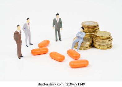 A miniature figurine of a man sits on coins, next to him are pills and figurines of people. Medical business concept