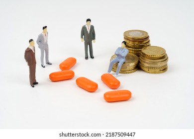 A miniature figurine of a man sits on coins, next to him are pills and figurines of people. Medical business concept