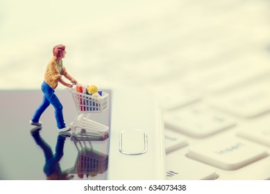 Miniature Figurine Of A Shopper Pushes A Shopping Cart On Smarthphone. Concept Of Brick And Mortar Stores Nowadays Face With Increased Competition From Online Ecommerce And Decreasing In Foot Traffic.