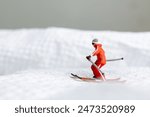 A miniature figurine of a skier dressed in vibrant winter gear. The skier is captured in motion, skiing across a white snowy landscape