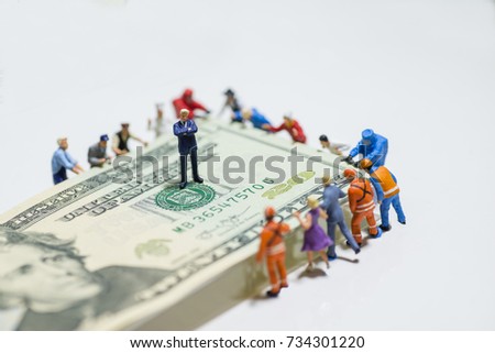 Miniature figurine toys holding US twenty dollar notes - slave to money and work concept. Focus on the businessman folding arms in the centre. Ruthless and slave to work concept.