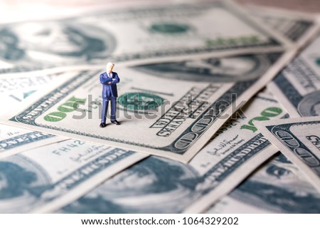 Miniature figurine toys standing on dollar with money and work concept. Focus on the businessman.
