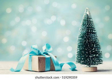 Miniature Fir Tree And Christmas Gift Box Against Blue Bokeh Background. Holiday Greeting Card.