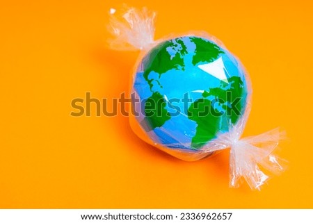 Miniature globe model wrapped in plastic, resembling a candy. Plastic pollution and waste related background with copy space.