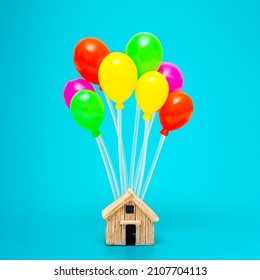 Miniature house with a bunch of multicolored balloons isolated on a blue background.