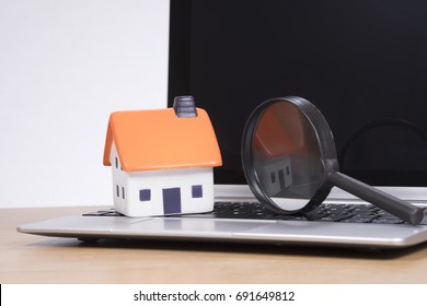 Miniature of house with magnifying glass standing on open laptop - Shutterstock ID 691649812