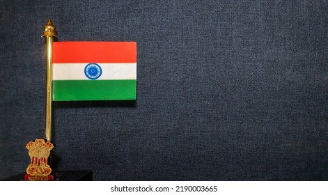 Miniature Indian National Flag On A Metal Stand With National Emblem 'Ashok Stambh' On Blue Canvas Background With Copy Space For Text.