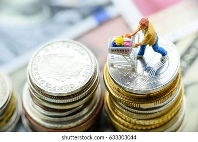 Miniature Of Male Consumer Pushes A Shopping Cart On Stacks Of Coins. Concept Of Brick And Mortar Stores Nowadays Face With Increased Competition From Online Ecommerce And Decreasing In Foot Traffic.