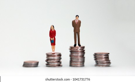Gender wage difference concept. A miniature man and a woman standing on top of a pile of coins.